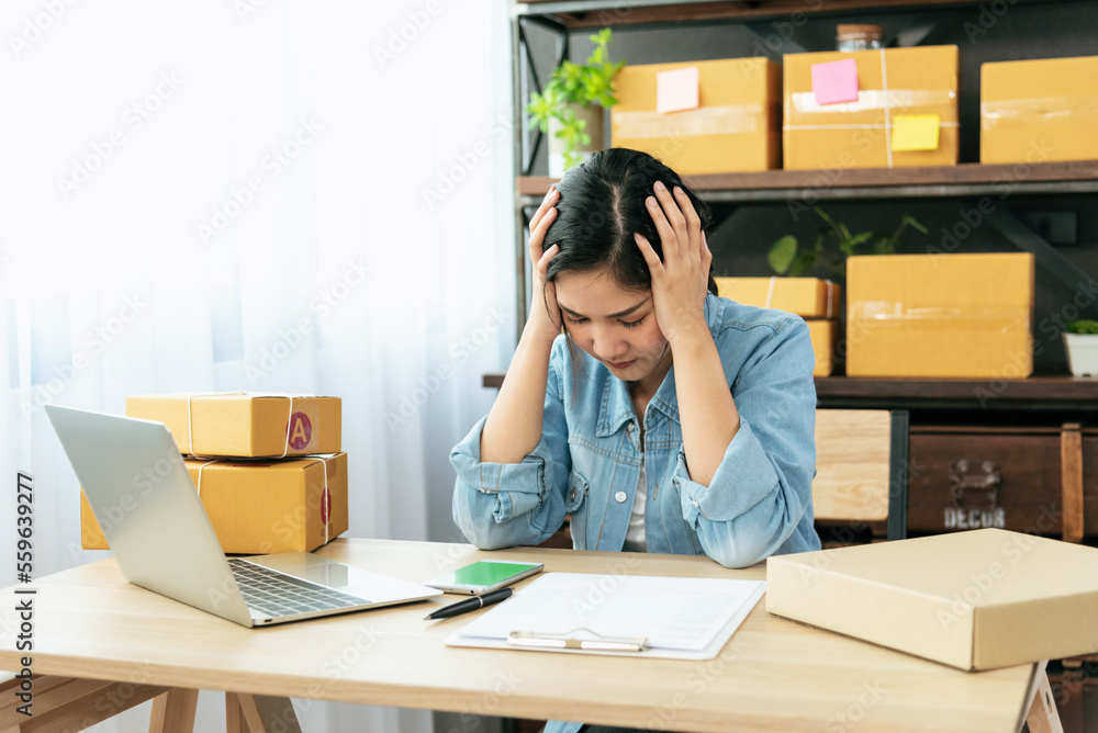 Desperate Asian woman stress headache depressed from startup small business at home office. Failure business woman work at home office. Online seller entrepreneur has problem delivery unhappy job - obrazy, fototapety, plakaty 