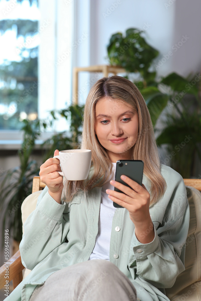 Woman with smartphone and cup of drink sitting in armchair at home Woman with smartphone and cup of drink sitting in armchair at home