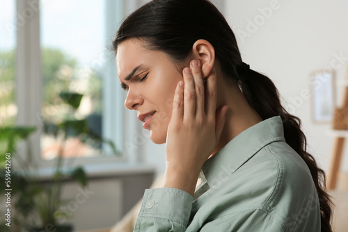 Young woman suffering from ear pain in room photo