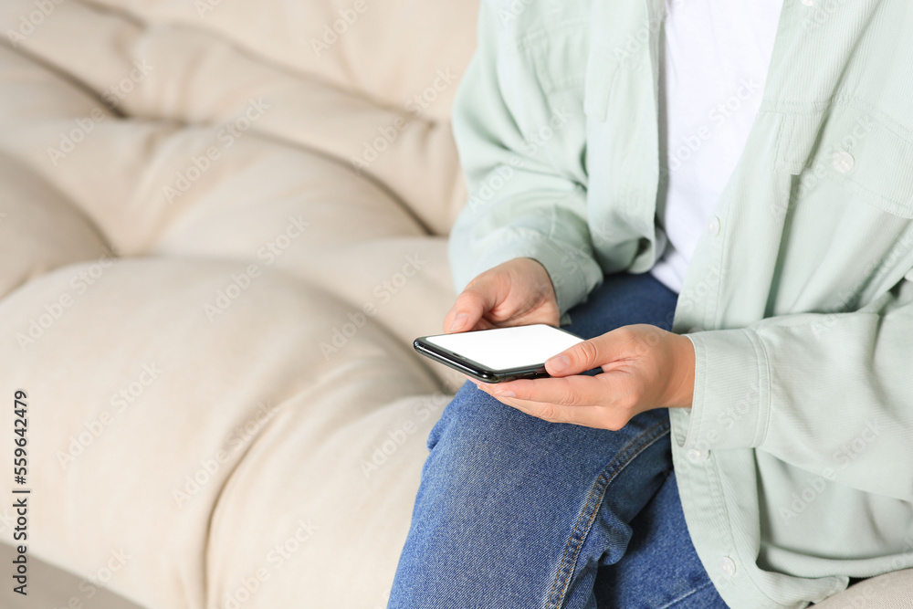 Woman using smartphone on sofa at home, closeup. Space for text