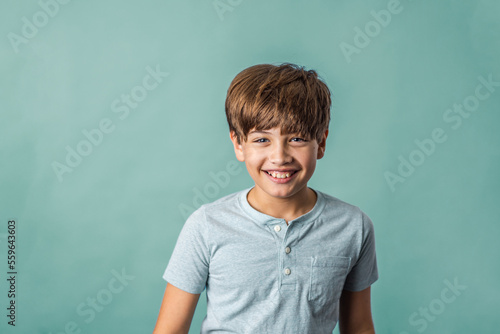 A cute pre-teen tween boy from the shoulders up on a muted green backdrop