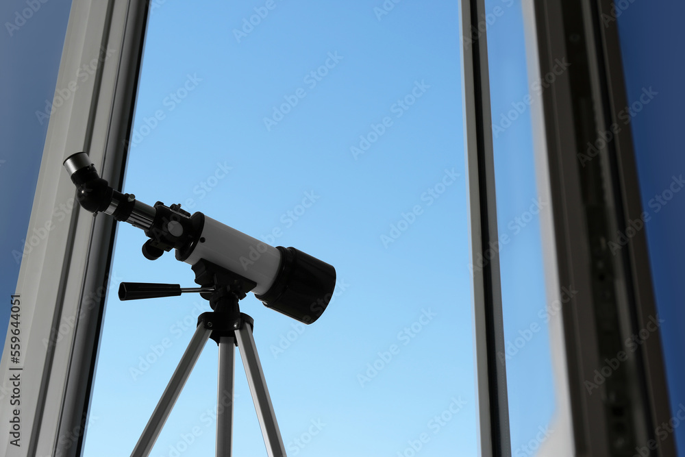 Tripod with modern telescope near open window indoors, low angle view. Space for text Tripod with modern telescope near open window indoors, low angle view. Space for text