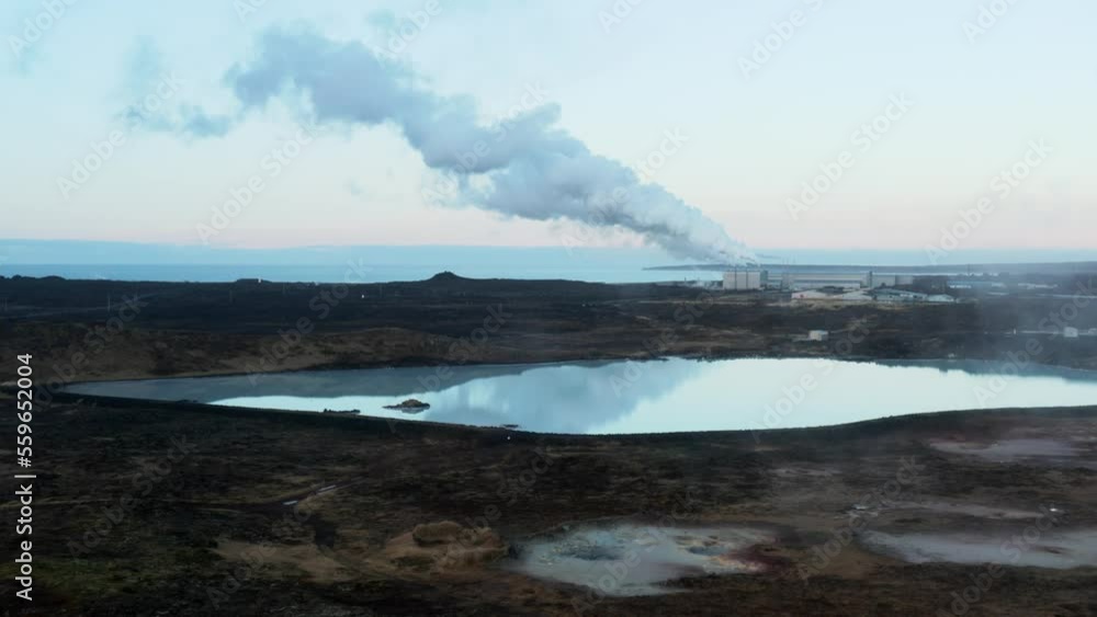White milky silica run off pool in Iceland with distant smoke coming from power plant White milky silica run off pool in Iceland with distant smoke coming from power plant