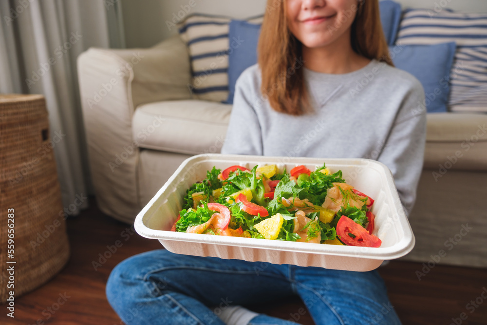 Closeup image of a young woman eating salad in paper box for takeaway food at home