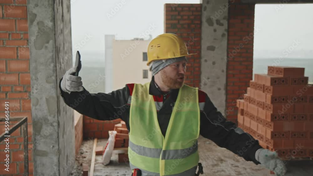 Medium tracking shot of bearded Caucasian foreman working at multistory construction site having video call with co-worker Medium tracking shot of bearded Caucasian foreman working at multistory construction site having video call with co-worker