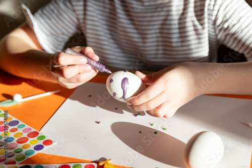 Child paints white egg. Creativity with children. girl's hands with eggs on the background of a table with paints, brushes, eggs, holiday flags.do-it-yourself. Handicrafts and crafts for Easter. DIY