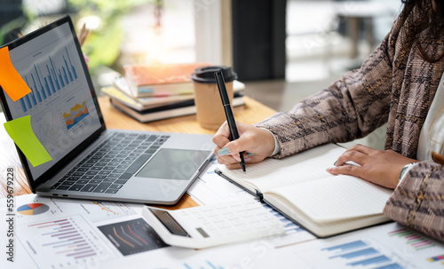 young woman in casual wear writing business papers at desk in modern coworking office.