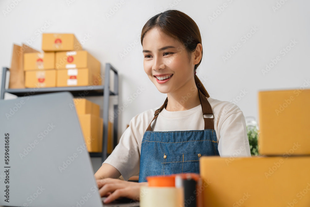 Startup small business, Young Asian woman checking online order on digital laptop and packing boxes for products to send to customers. working at the home office. Startup small business, Young Asian woman checking online order on digital laptop and packing boxes for products to send to customers. working at the home office.