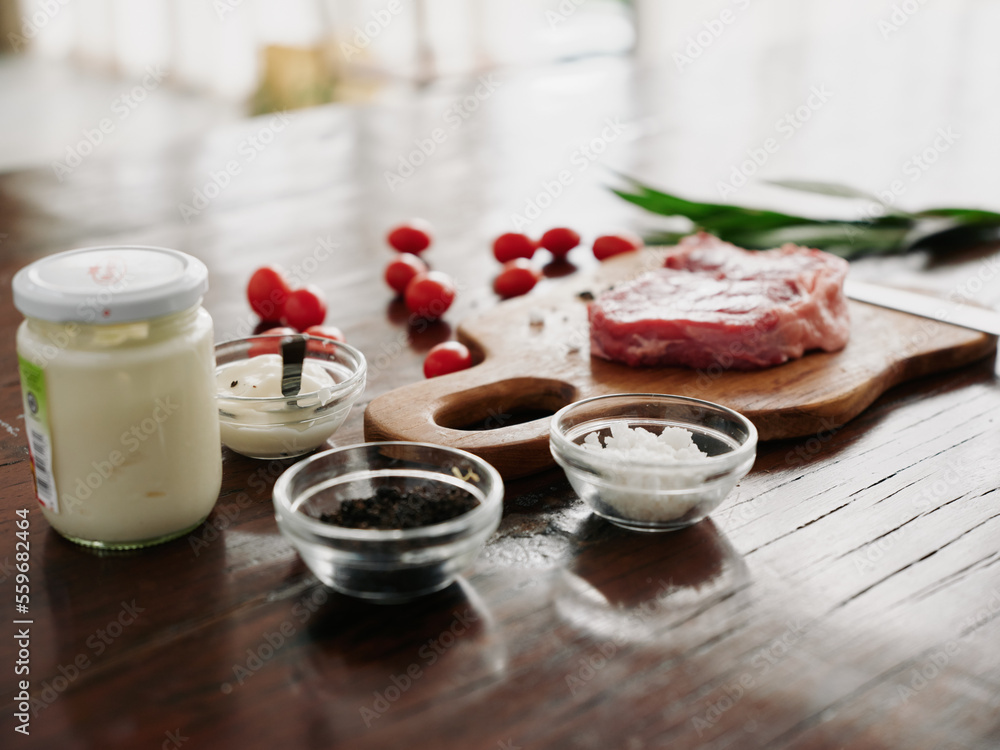 Stylish kitchen, on a wooden table there is a piece of fresh meat with spices, tomatoes and herbs, firelight from the window. Stylish kitchen, on a wooden table there is a piece of fresh meat with spices, tomatoes and herbs, firelight from the window.
