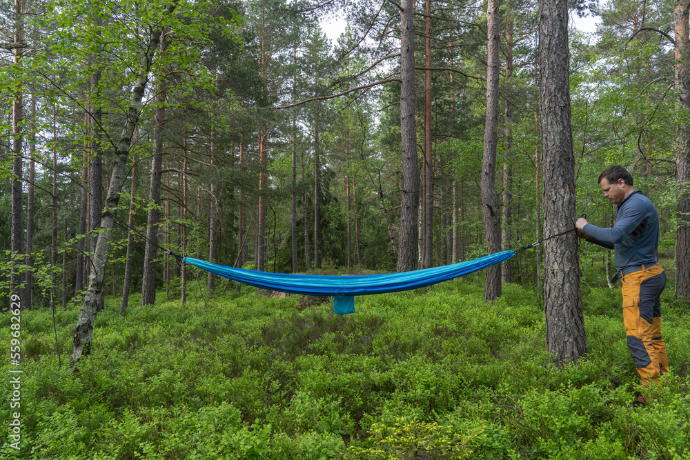 A man standing near hammock in the forest.