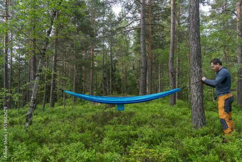 A man standing near hammock in the forest.