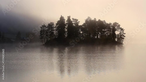 Small island on the lake. Moody autumnal morning with flowing fog above the lake surface. Jonsvatnet lake in Norway. photo