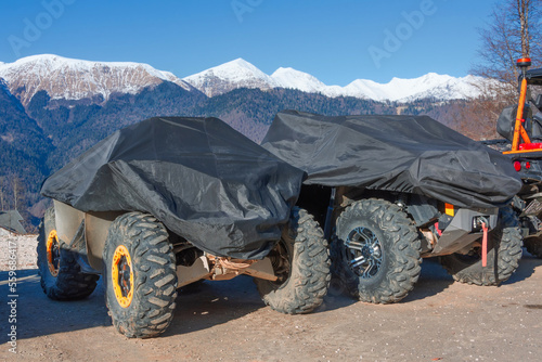 Shelter with a protective cover with a tarpaulin off-road vehicles stand against the backdrop of snow-capped mountains.