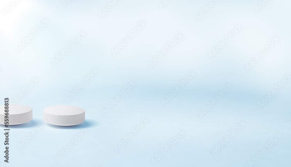 Two white pills lying on a blue table. Two white pills lying on a blue table.