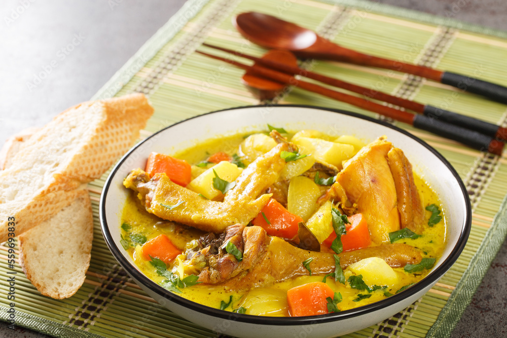 Coconut chicken curry with potatoes, onions and carrots served with a baguette close-up on a mat on the table. Horizontal Coconut chicken curry with potatoes, onions and carrots served with a baguette close-up on a mat on the table. Horizontal