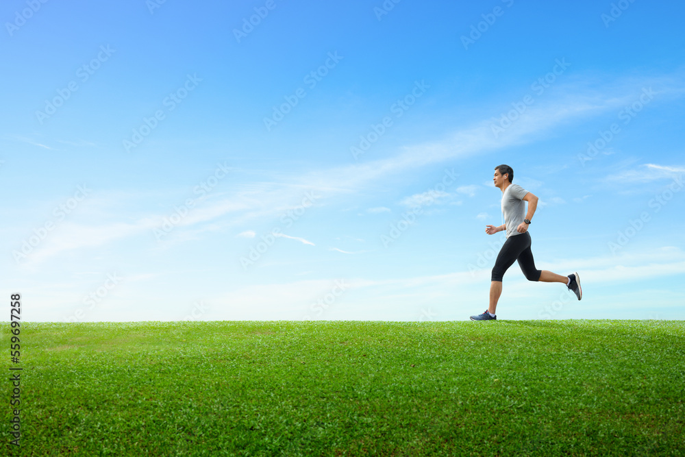 Side view of asian man jogging on spring grass field with clear blue sky background. Side view of asian man jogging on spring grass field with clear blue sky background.