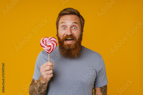 Bearded man holding lollipop while standing isolated over background