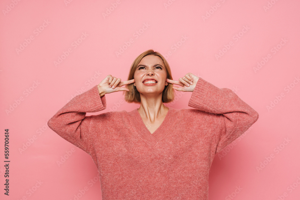Young woman blocking her ears with irritation and looking up at copy space isolated over pink background Young woman blocking her ears with irritation and looking up at copy space isolated over pink background