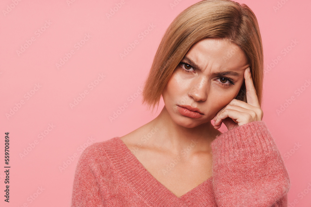 Pensive blonde woman touching her temple isolated over pink background Pensive blonde woman touching her temple isolated over pink background