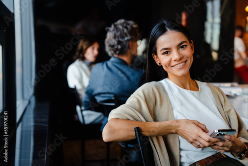 Hispanic young woman smiling and using cellphone during offline meeting