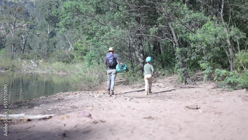 A father and son walk along a river bank in Australia while carrying a traditional swag for camping. photo