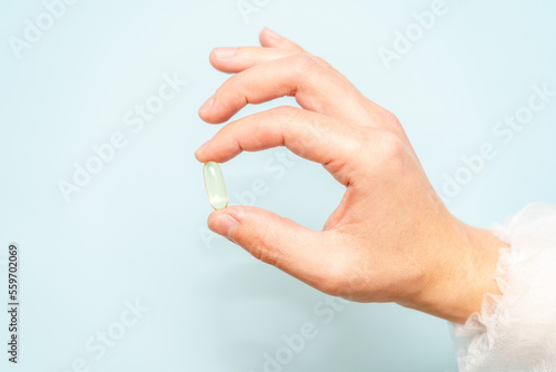 Doctor's hand holding a fish oil capsule (Omega 3) or pill isolated on light blue background