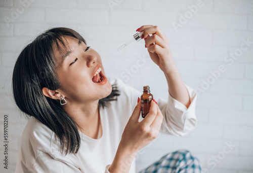 Asian woman dripping cbd oil into her mouth. Close up asian women taking CBD Oil for sleep. Medical cannabis. Vitamins and supplements photo