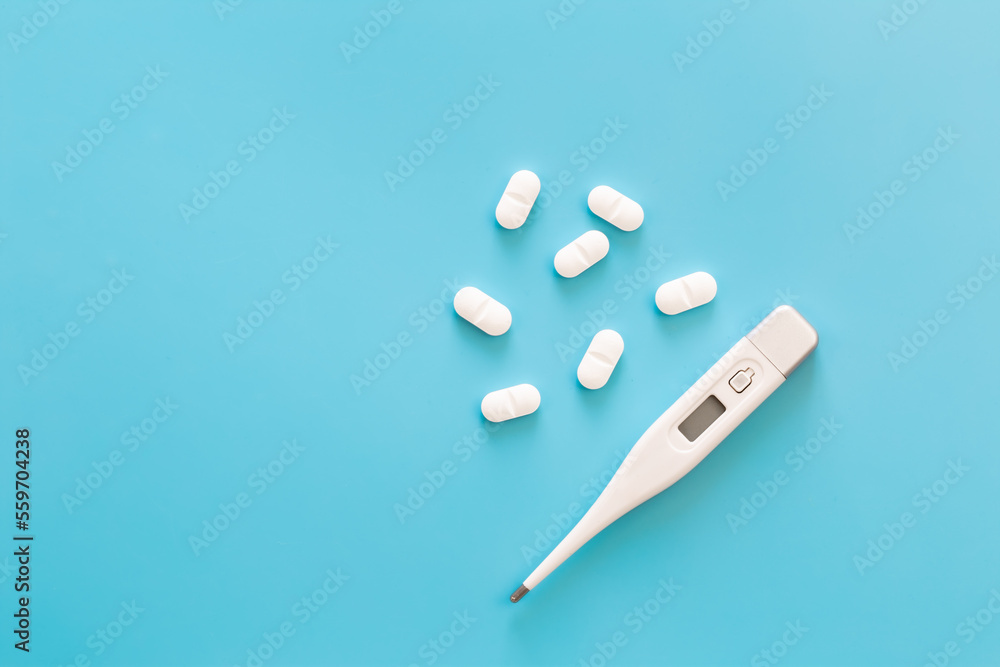 Pills and electronic thermometer on a blue background, flat lay. Pills and electronic thermometer on a blue background, flat lay.
