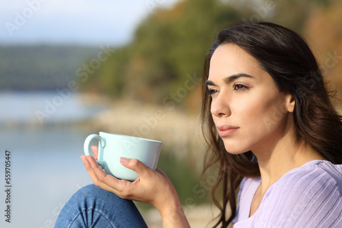 Serious woman drinking coffee looking away in nature