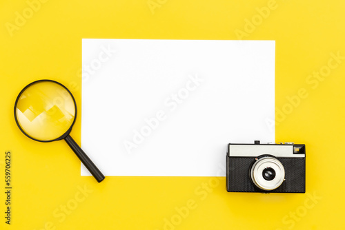 Minimal background with blank paper, camera and magnifier, flat lay.
