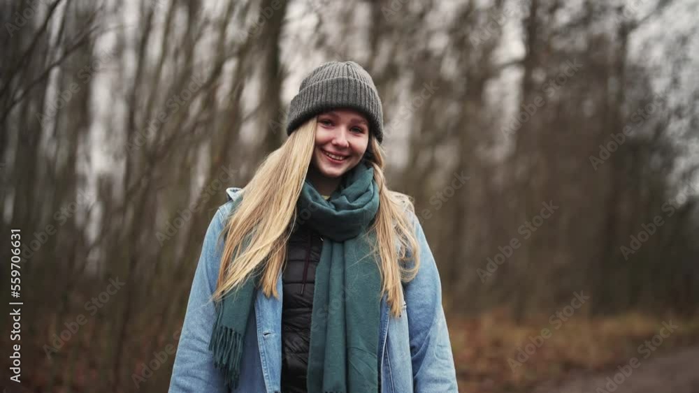 Girl traveler walks in forest or park in autumn clothes against trees, looks at camera and toothy smile. Portrait of happy female enjoy hike in nature outdoors. Beautiful model posing alone. Girl traveler walks in forest or park in autumn clothes against trees, looks at camera and toothy smile. Portrait of happy female enjoy hike in nature outdoors. Beautiful model posing alone.