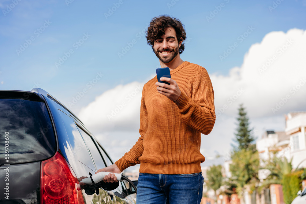 © Westend61 - Happy man using smart phone and charging car at vehicle charging station
