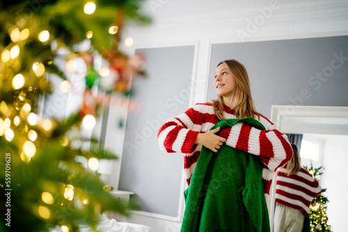 Smiling girl holding green sweater with Christmas tree in foreground photo