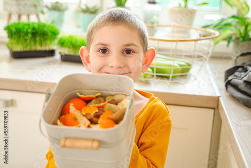 Smiling boy holding compost bucket of orange peels at home photo