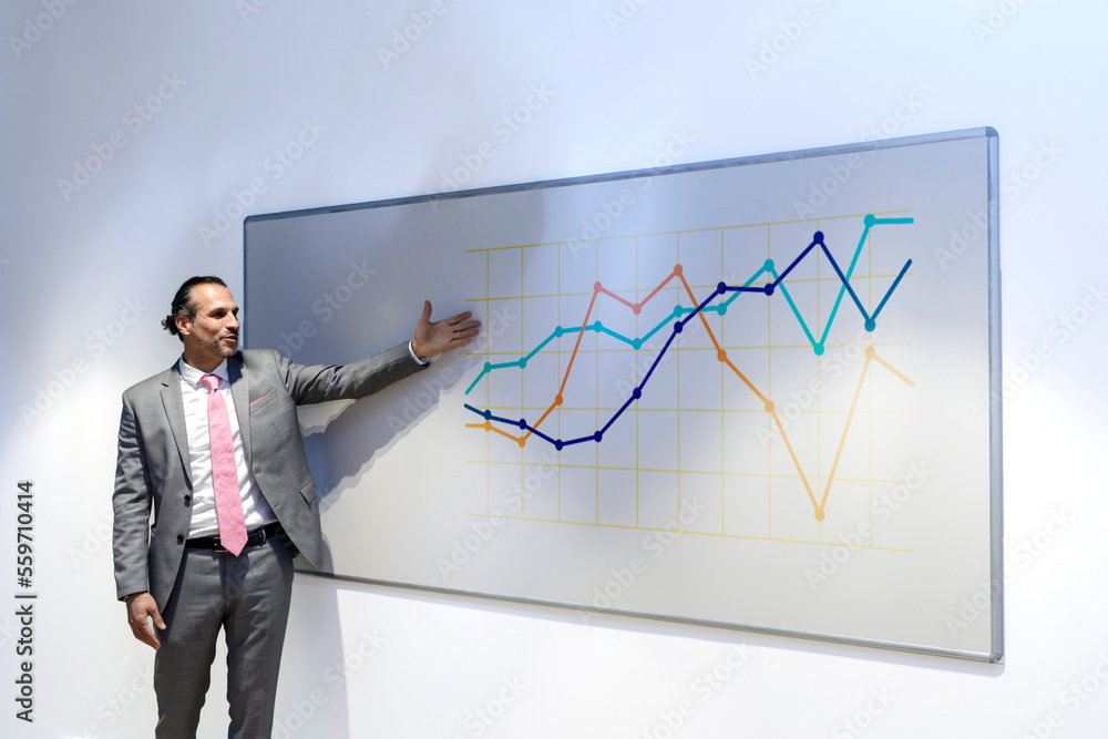 Mature businessman showing graph on whiteboard in conference room at office Mature businessman showing graph on whiteboard in conference room at office