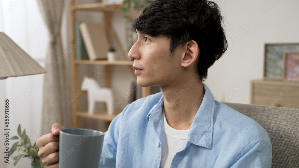 Fototapeta premium cheerful asian japanese young male looking out of window and enjoying the tranquil morning and coffee from cup in the living room at home