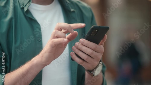 Close-up view of attractive young caucasian man's hands using smartphone online checking social media making internet payments. Focused modern adult male typing texting scrolling on phone outside.