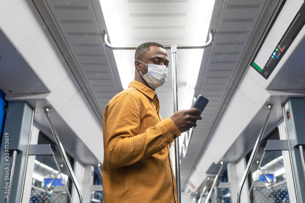 A businessman in a protective mask with a mobile phone rides in a subway car to the office