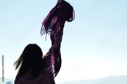 Woman raising a lilac feminist scarf in protest against gender violence. Free blue background. Focus on the lilac scarf
