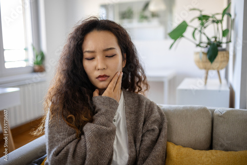 Portrait of unhappy young Asian woman suffering from toothache at home. Healthcare, dental health and problem concept.