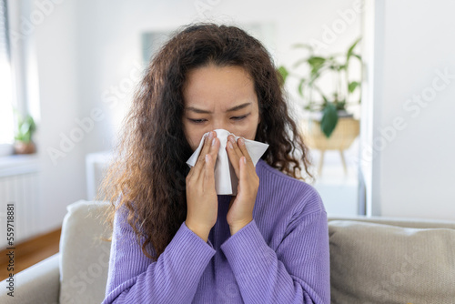 Sick desperate Asian woman has flu. Rhinitis, cold, sickness, allergy concept. Pretty sick woman has runnning nose, rubs nose with handkerchief. Sneezing female. Brunette sneezing in a tissue