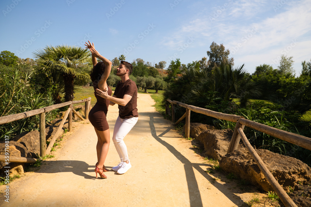 Obraz premium Handsome young man and woman dancing bachata and salsa in the park. The couple dance passionately surrounded by greenery. Dancing concept.