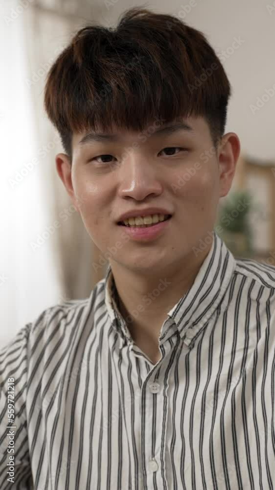 Vertical Screen: shoulder shot portrait of cheerful asian businessman turning head and looking at camera with a smiling face while working from home on laptop in the living room Vertical Screen: shoulder shot portrait of cheerful asian businessman turning head and looking at camera with a smiling face while working from home on laptop in the living room