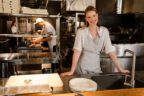 Young chef woman standing by sink while working in restaurant kitchen