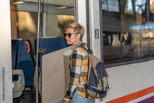 Adult 35s year old lesbian woman in plain shirt and jeans with backpack and sunglasses traveling by train in Europe. Train station in Barcelona, Spain.