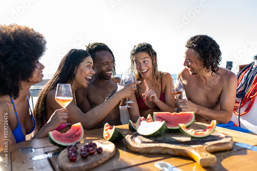 Friends toasting drinks in boat party  smiling people with glasses of champagne on yacht  five multiracial young friends celebrating holiday during a luxury journey on sail