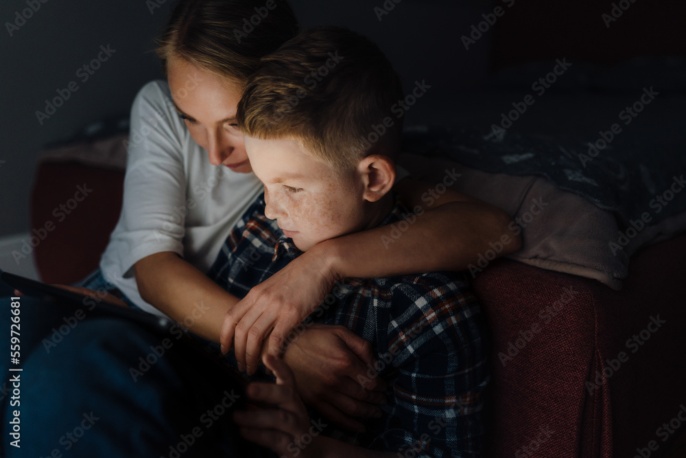 Young mother hugging her son while he's using tablet computer at home Young mother hugging her son while he's using tablet computer at home