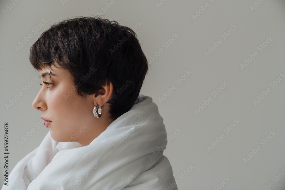 Profile of young woman wrapped in blanket standing indoors Profile of young woman wrapped in blanket standing indoors