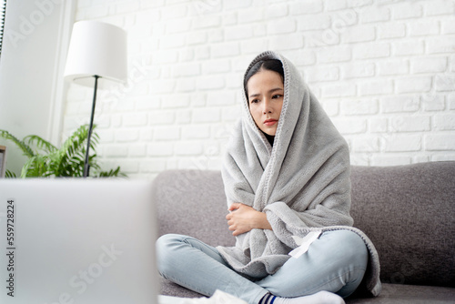 Obraz na płótnie Upset young woman freezing, feeling cold at home, sitting on sofa covered with b
