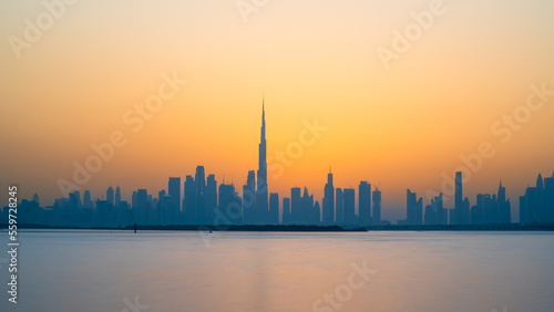 A stunning view of the Dubai skyline at sunset  as seen from the water. The golden light reflects on the skyscrapers and the Burj Khalifa  the world s tallest building. 